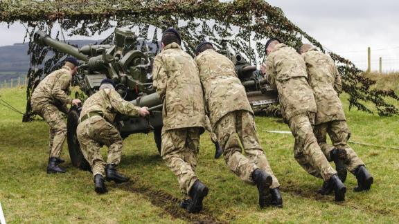 Armed forces personnel in camouflage uniform moving artillery equipment during a training exercise.