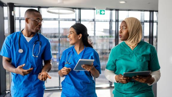 Three diverse nurses in conversation whilst walking down a hospital corridor