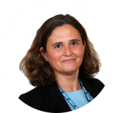 Caroline Julien headshot wearing a black blazer, light blue top with shoulder length brown hair against a white background