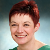 Kirsten Major smiling wearing a green top, red hair and a faded green background
