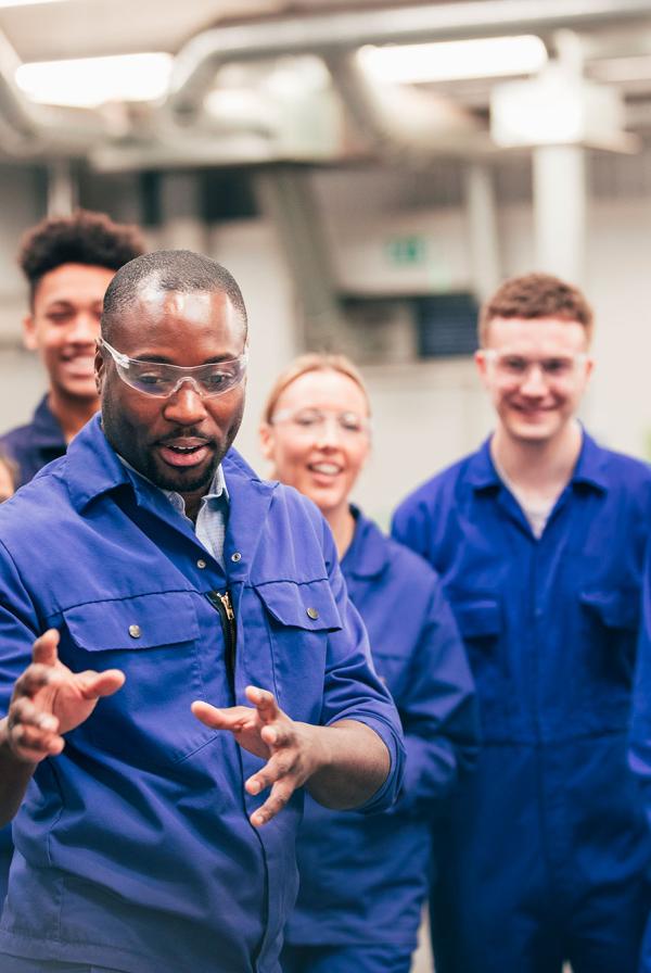 A diverse group of apprentices, wearing boiler suits, being taught
