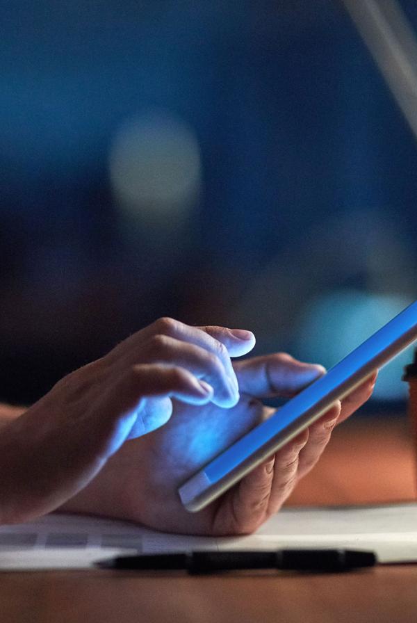 Someone using a tablet at a desk lit by a lamp.