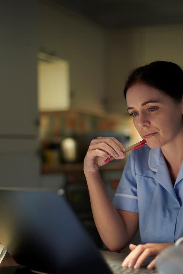 Healthcare worker working on a laptop in a softly lit room. 