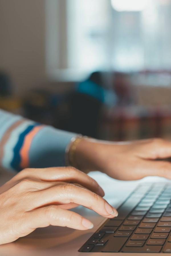 Close-up of hands typing on a laptop keyboard at a desk in an indoor setting.