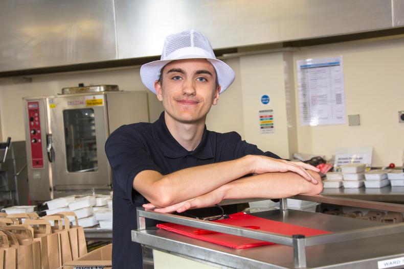 An apprentice caterer leaning on kitchen equipment.