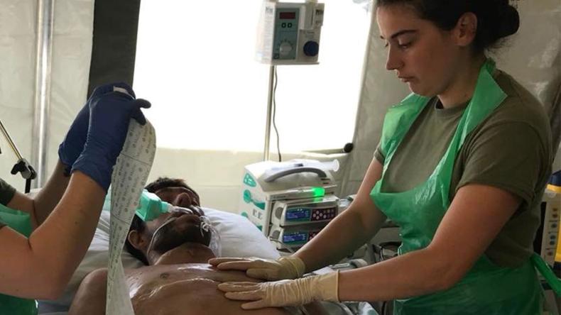 Army Reservist treating a patient on a hospital bed with medical equipment nearby
