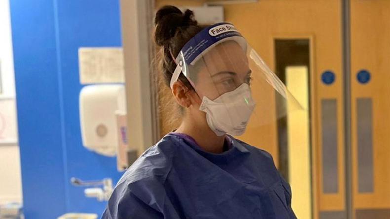 Female healthcare worker in full PPE standing in a hospital setting