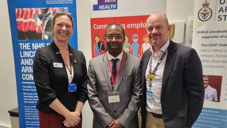 Three people pose in front of Step into Health branded banners at an event.