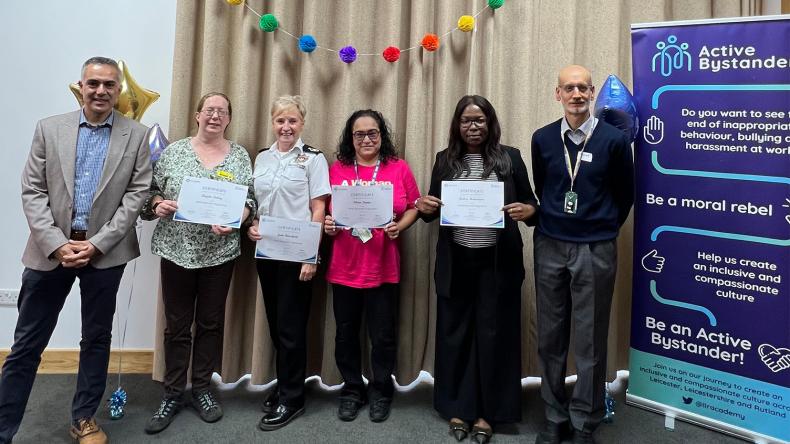 Do OD Active Bystander Programme - a group of people posing for a photo in front of a display board holding certificates.